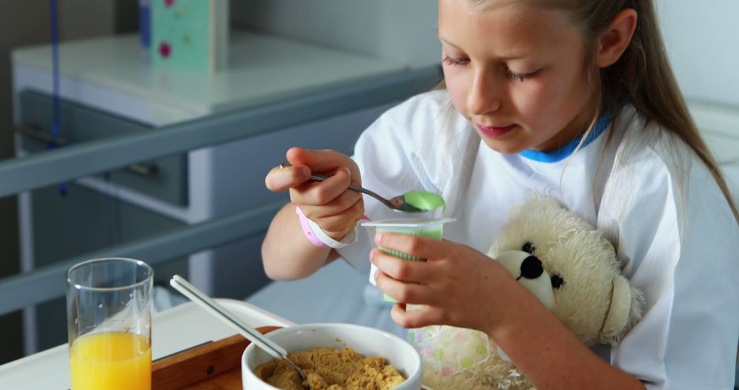 Young Girl Eating Breakfast in Hospital Bed While Holding Teddy Bear - Free Images, Stock Photos and Pictures on Pikwizard.com