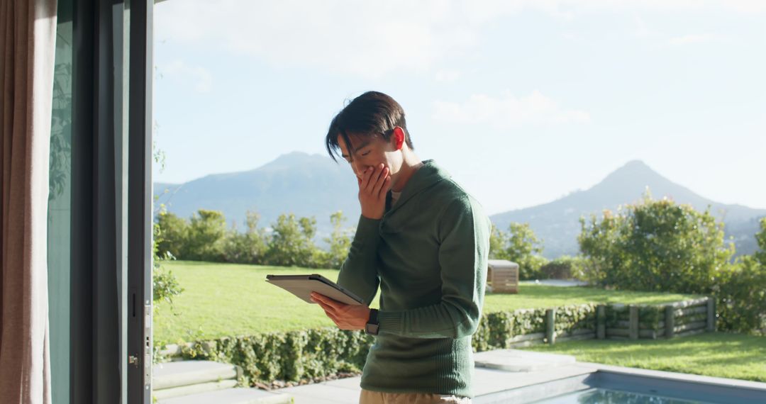 Man Holding Tablet Standing Outside Near Pool Experiencing Outdoor Serenity