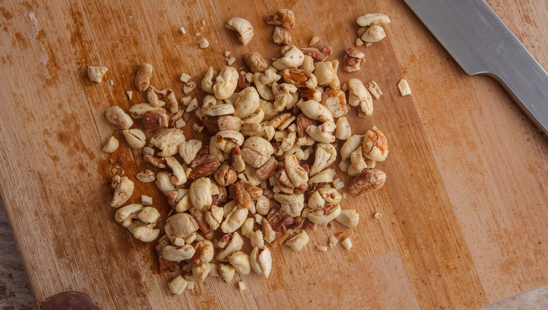 Chopping assorted nuts on rustic wooden cutting board with chef knife, closeup texture