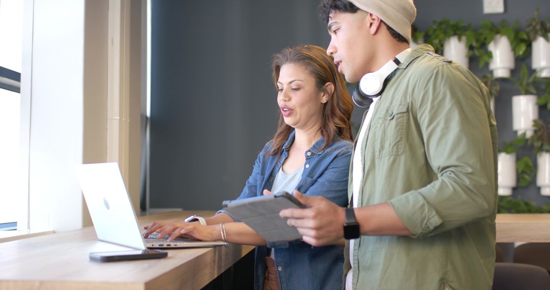 Coworkers collaborating at standing desk with laptop and tablet in modern coworking hub