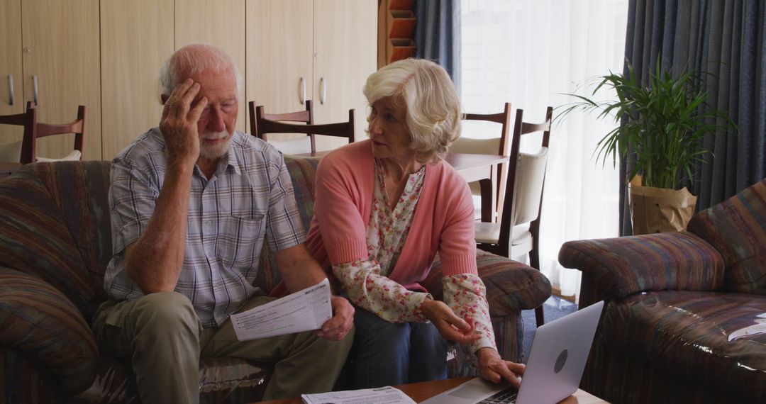 Senior Couple Reviewing Documents and Using Laptop on Couch