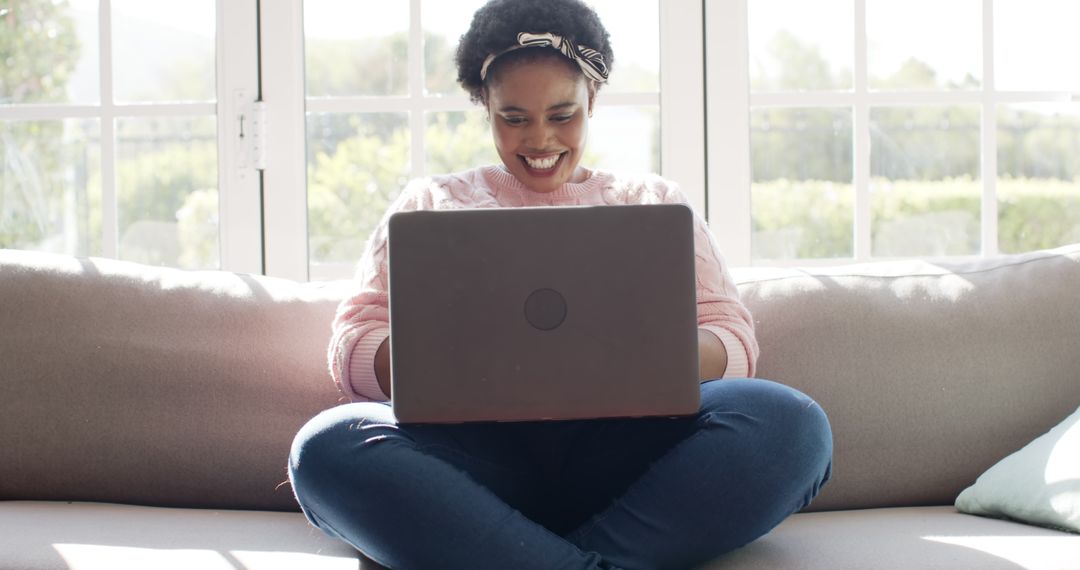 Content Woman Smiling While Using Laptop on Couch in Sunlit Room