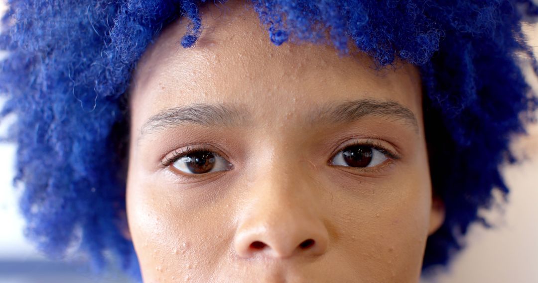 Portrait of biracial businesswoman with blue afro and brown eyes looking at camera at office - Free Images, Stock Photos and Pictures on Pikwizard.com