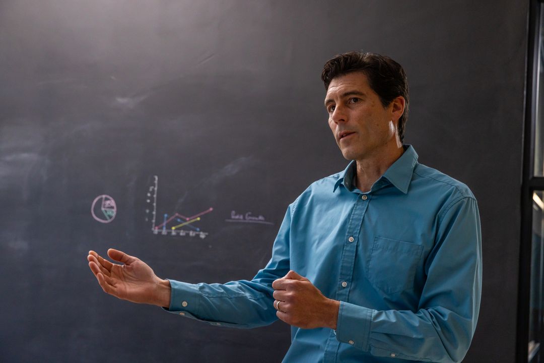 Male Educator Explaining Chart Diagrams on Chalkboard