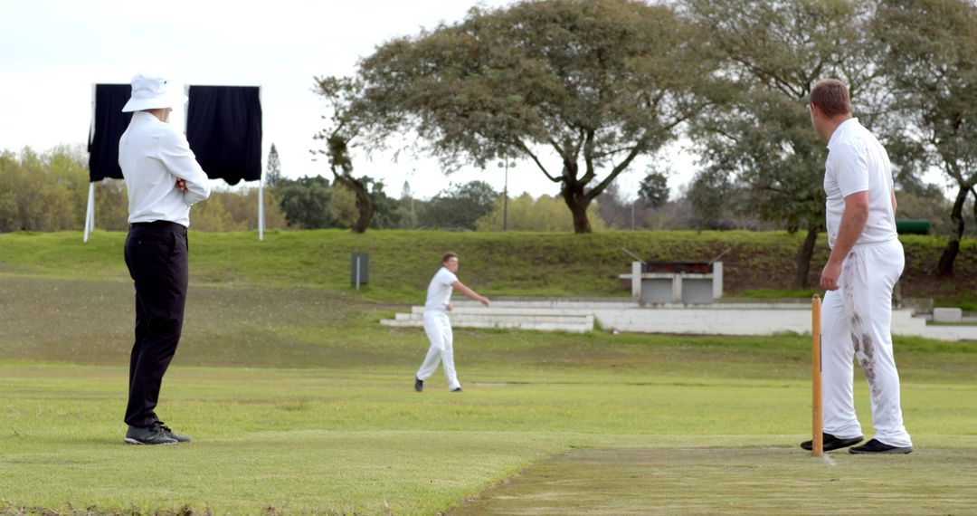 Men Engaged in Vigorous Cricket Match on Green Field