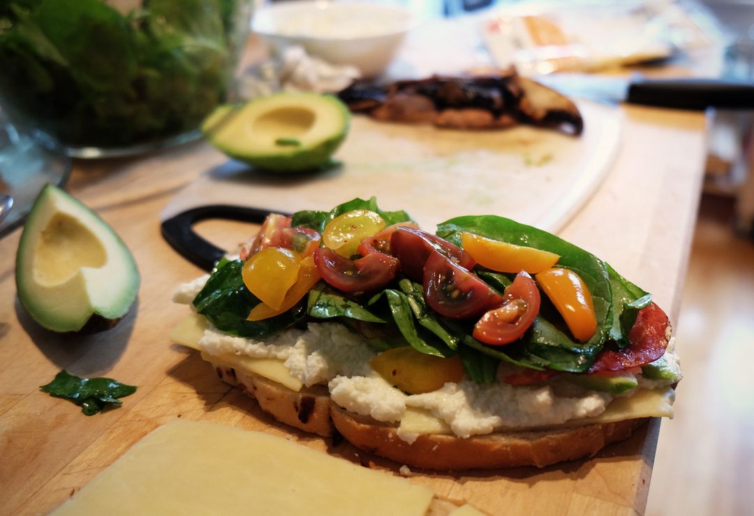 Open-Faced Avocado Ricotta Sandwich with Cherry Tomatoes and Spinach on Cutting Board