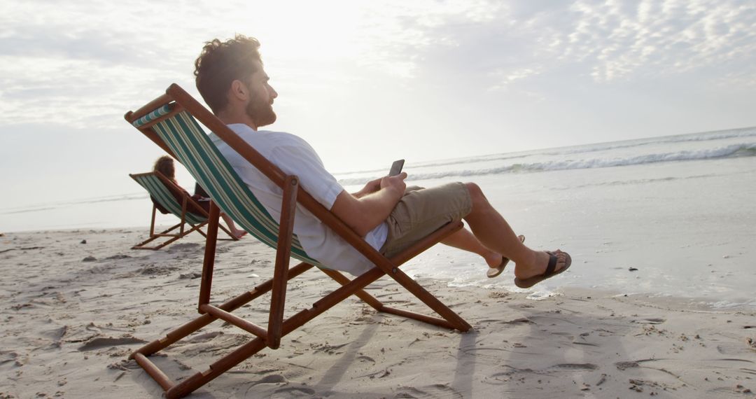 Man Relaxing on Beach Chair with Smartphone at Sandy Beach - Free Images, Stock Photos and Pictures on Pikwizard.com