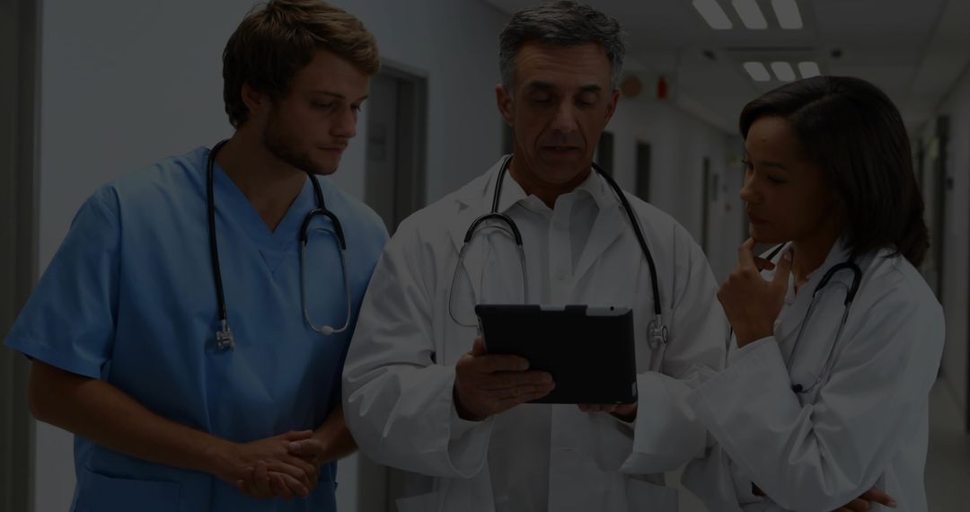 Medical Team Reviewing Patient Data on Tablet in Hospital Corridor for Clinical Collaboration