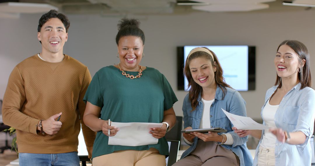 Diverse team collaborating in modern office holding tablet and documents, smiling