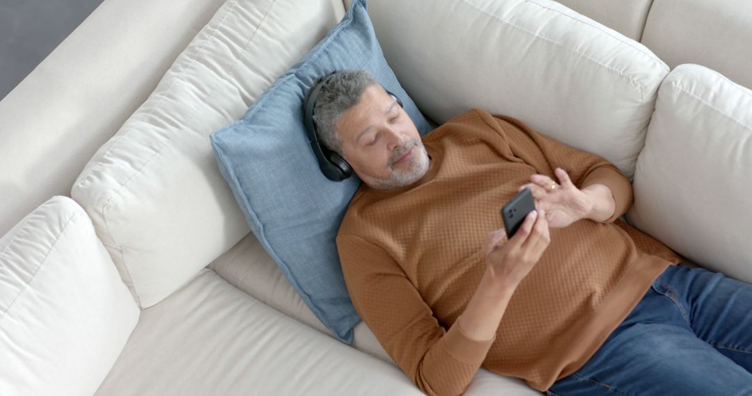 Man Relaxing on Sofa with Smartphone and Headphones - Free Images, Stock Photos and Pictures on Pikwizard.com