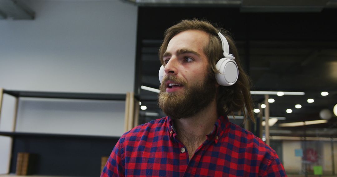 Young Man with Beard Listening to Music on Headphones in Modern Office - Free Images, Stock Photos and Pictures on Pikwizard.com