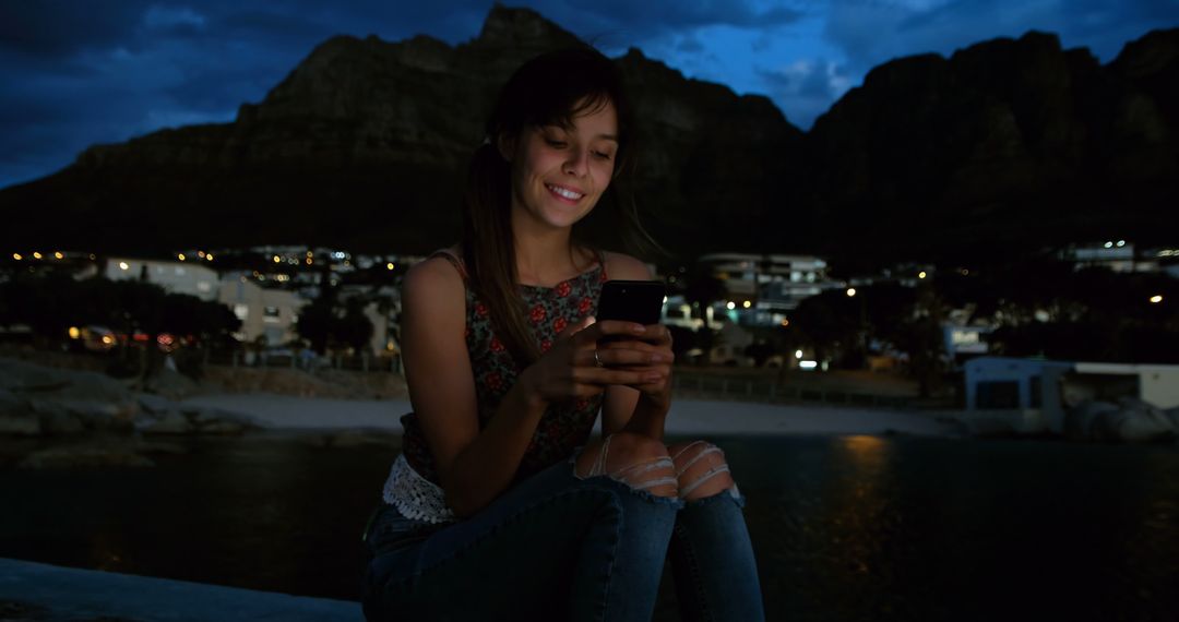 Young Woman Smiling While Using Smartphone Outdoors at Evening Time - Free Images, Stock Photos and Pictures on Pikwizard.com