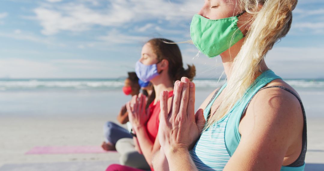 Group of diverse female friends wearing face masks meditating at the beach - Free Images, Stock Photos and Pictures on Pikwizard.com