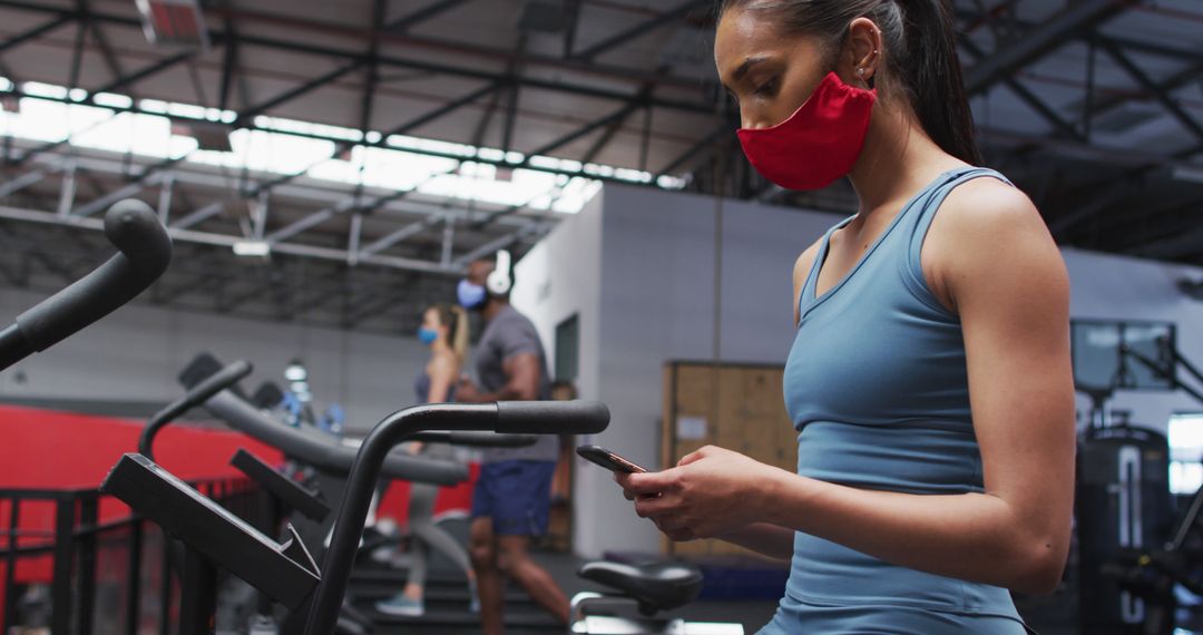 Woman Exercising at Gym with Face Mask While Using Smartphone - Free Images, Stock Photos and Pictures on Pikwizard.com