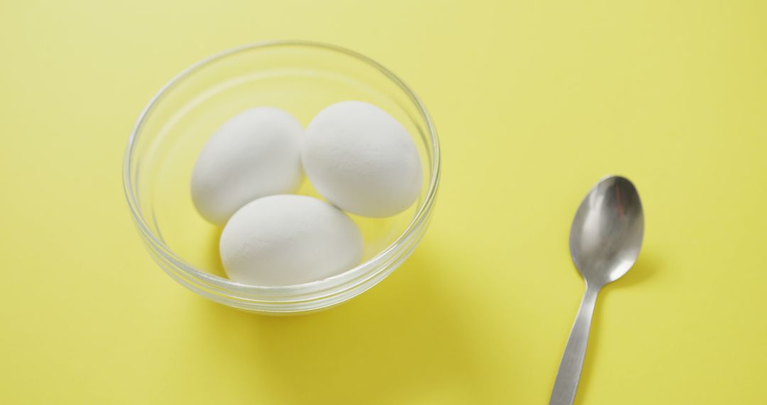 Three White Eggs in Glass Bowl with Spoon on Yellow Background - Free Images, Stock Photos and Pictures on Pikwizard.com