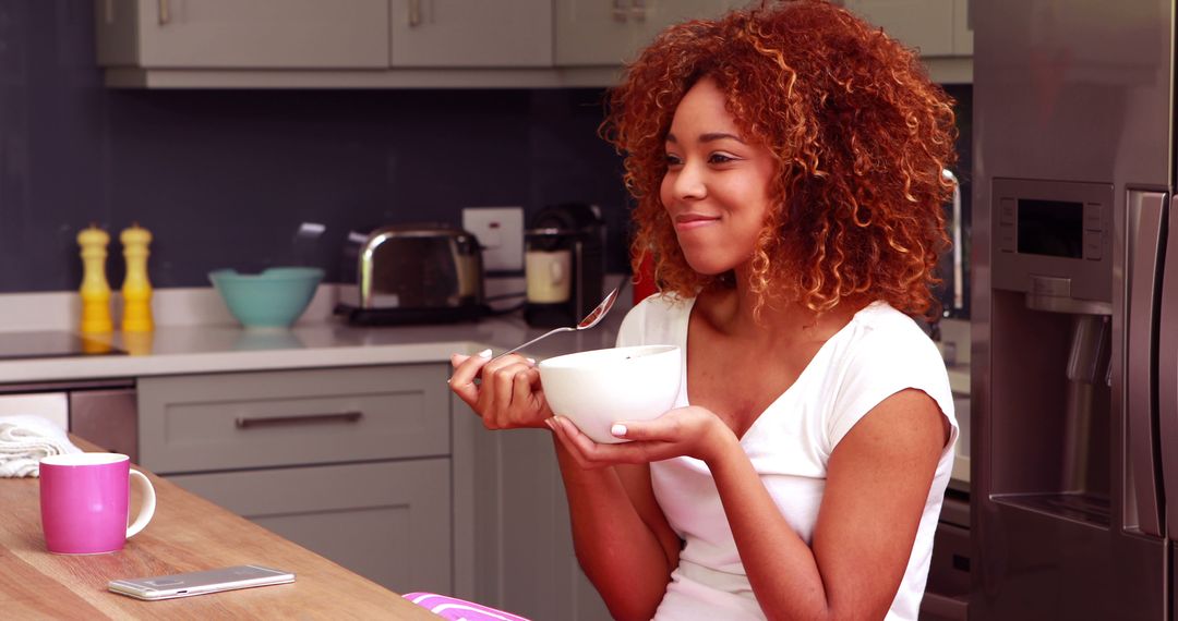 Smiling Woman Eating Breakfast Cereal in Modern Kitchen - Free Images, Stock Photos and Pictures on Pikwizard.com