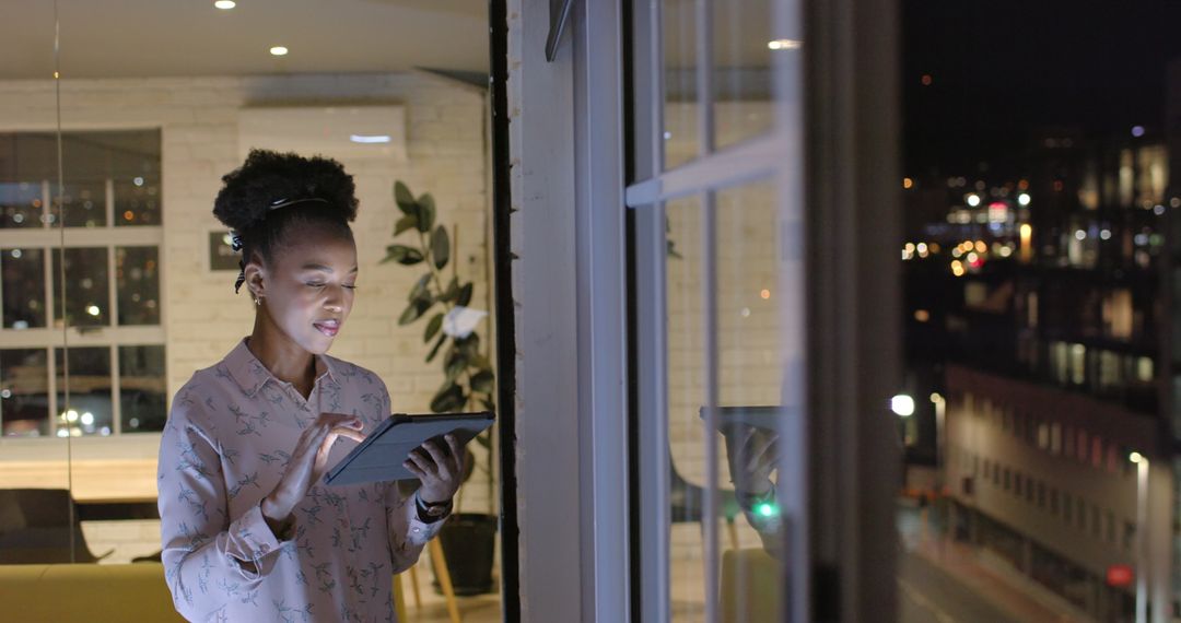 African American Businesswoman Using Tablet Near Window in Office at Night