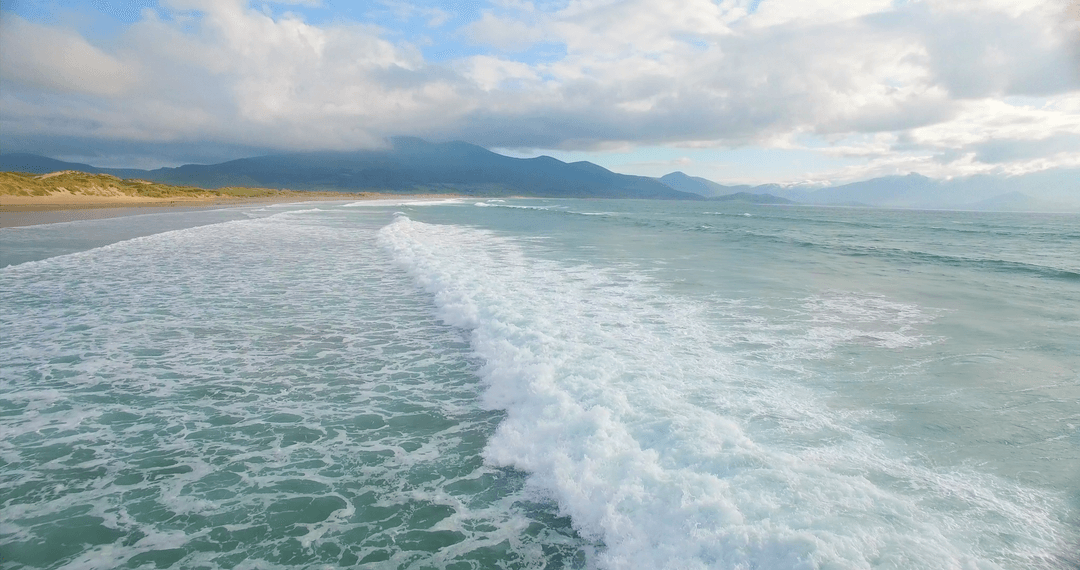 Transparent ocean waves meeting calm beach under clouded sky
