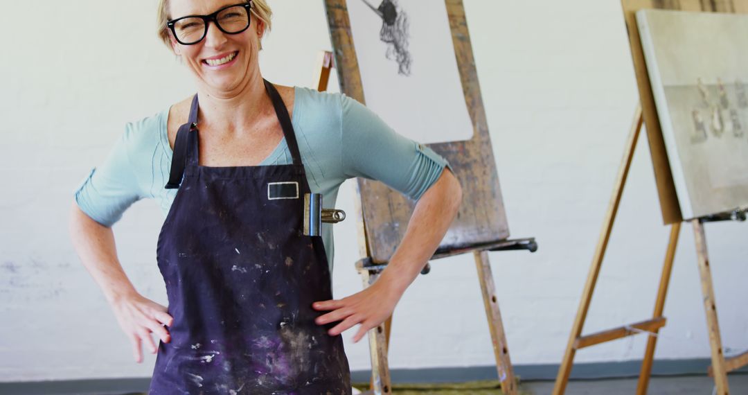 Confident Female Artist Smiling in Studio with Canvas Paintings - Free Images, Stock Photos and Pictures on Pikwizard.com