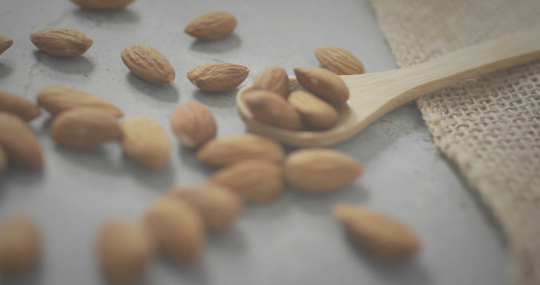 Wooden Spoon Holding Whole Almonds on Rustic Stone Slab with Burlap Texture, Closeup