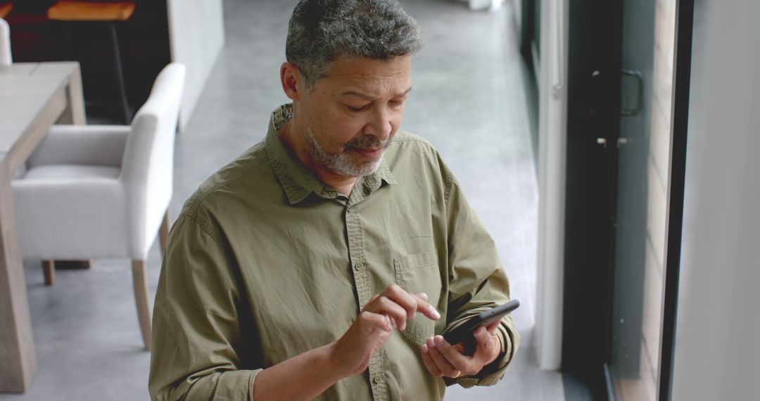 Middle-aged Man Focusing on Smartphone by Large Window - Free Images, Stock Photos and Pictures on Pikwizard.com