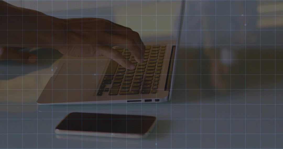 Hand Typing on Laptop Keyboard with Smartphone on Table