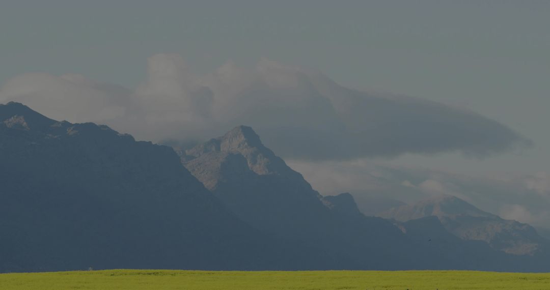 Layered Mountain Range Rising Above Green Meadow with Low Clouds and Morning Haze