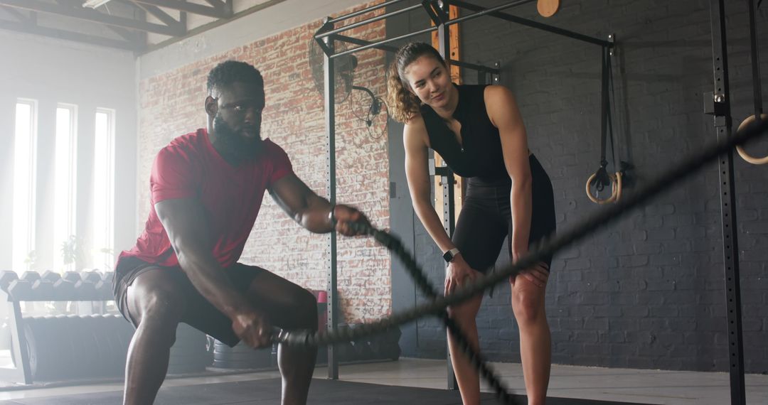 Personal Trainer Guiding Client on Battle Rope Exercise in Industrial Gym