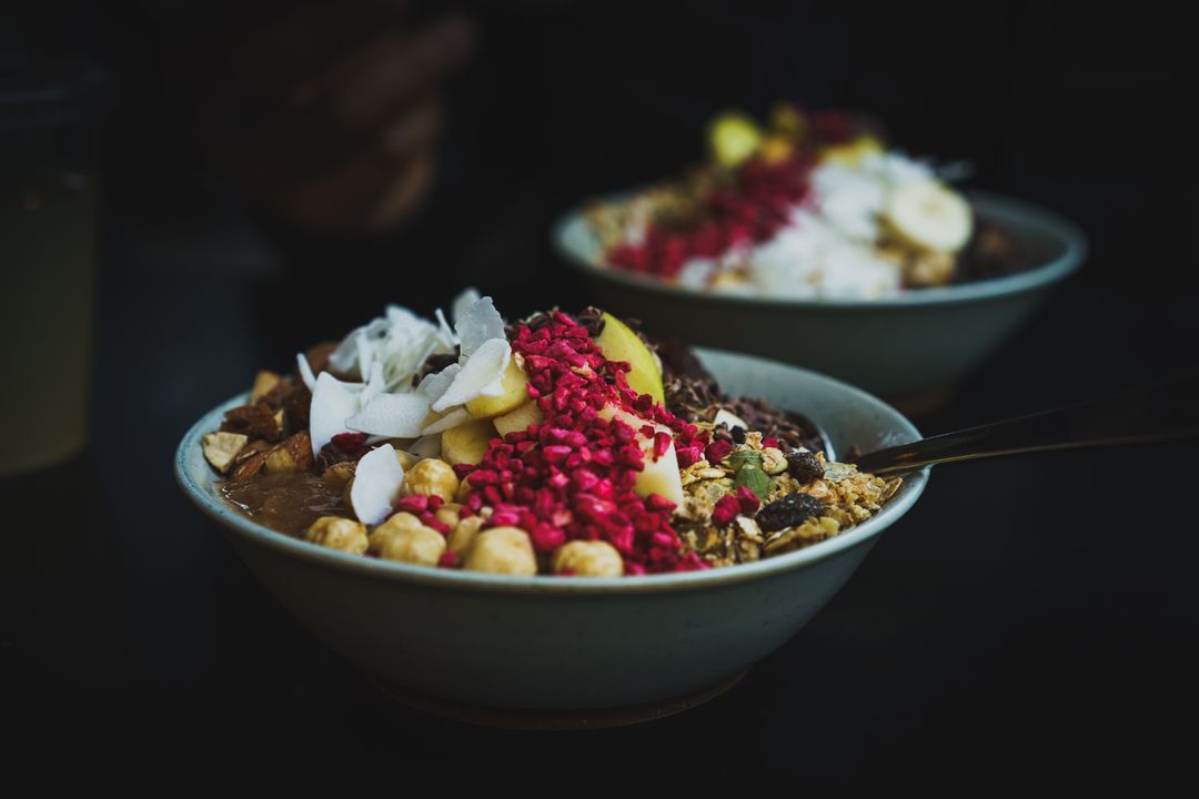 Serving colorful smoothie bowl overflowing with granola, banana, coconut flakes, raspberries