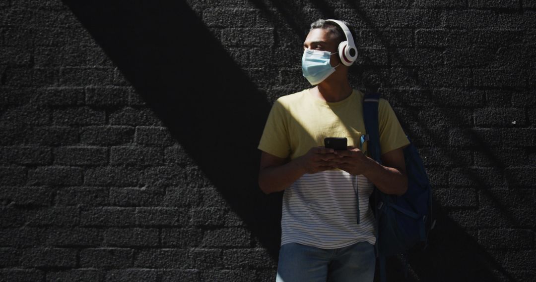 Man Wearing Mask and Headphones Using Smartphone