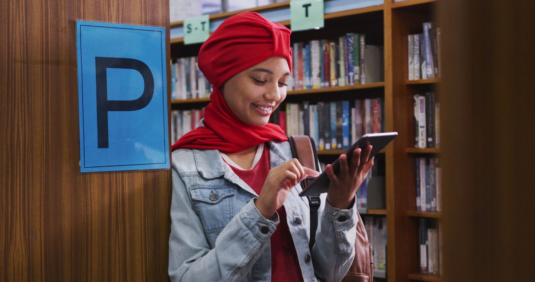 Smiling Woman Wearing Red Hijab Using Digital Tablet in Library - Free Images, Stock Photos and Pictures on Pikwizard.com