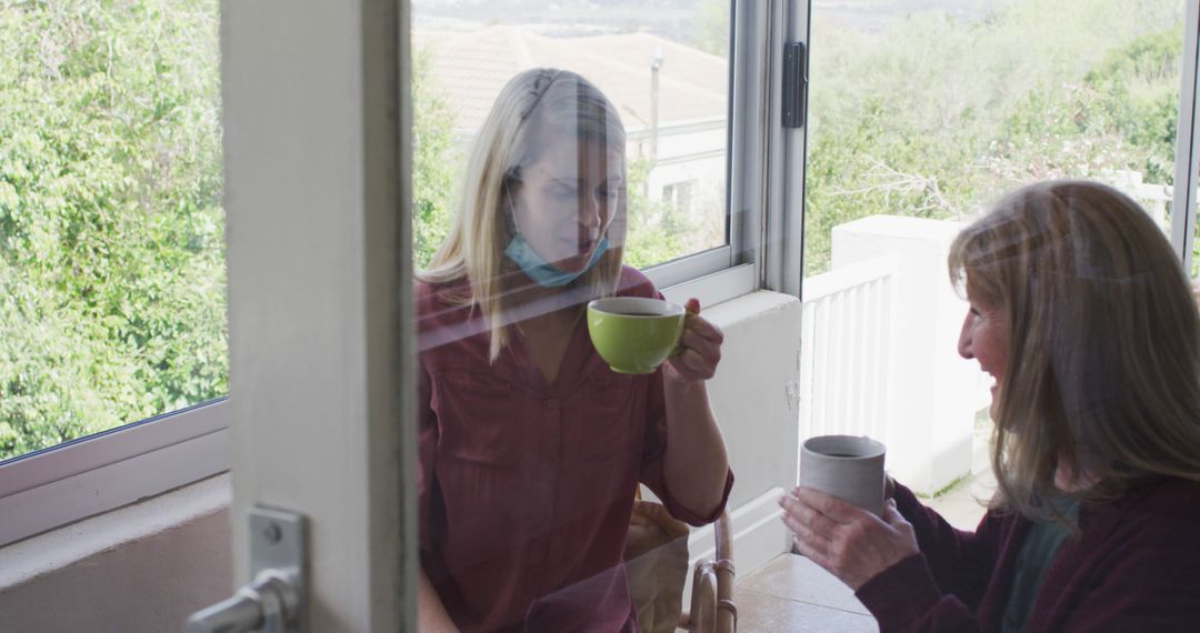 Two Women Socializing with Masks and Coffee Separated by Window - Free Images, Stock Photos and Pictures on Pikwizard.com