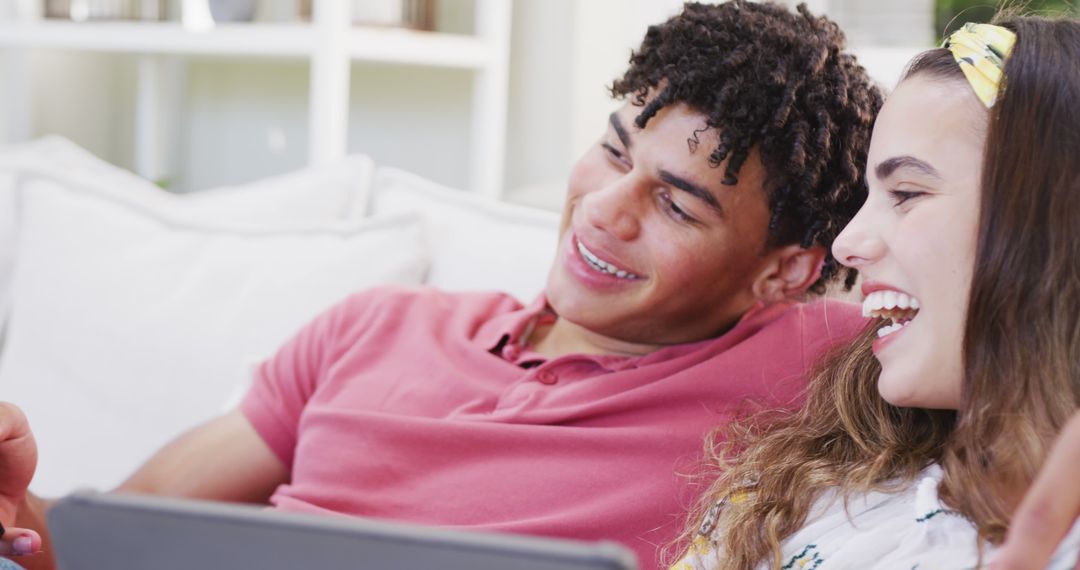 Joyful Young Couple Smiling While Using Gadgets at Home