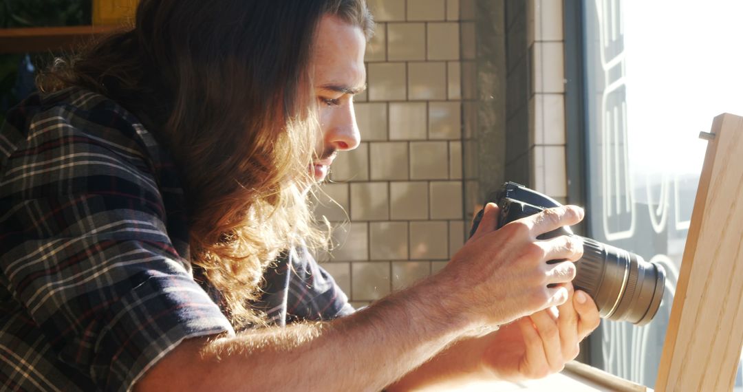 Male Photographer Using Camera in Brightly Lit Room with Long Hair - Free Images, Stock Photos and Pictures on Pikwizard.com