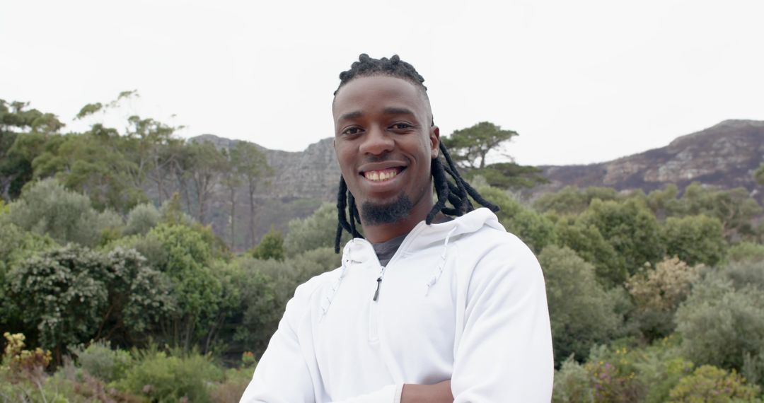 Confident African American man smiling with arms crossed wearing white hoodie outdoors