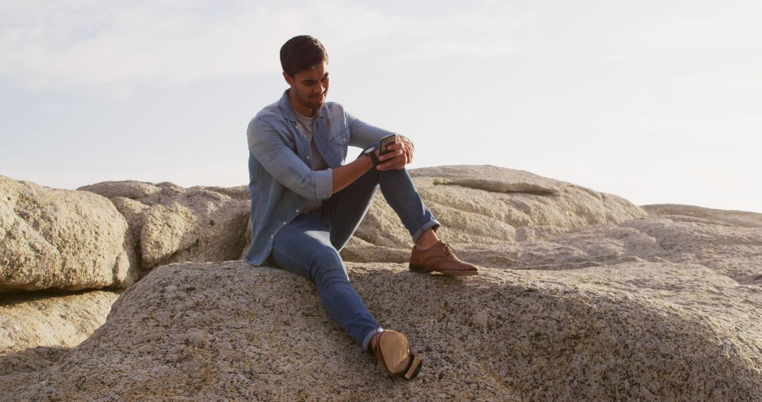 Man Relaxing on Rock Using Smartphone at Outdoor Scenic Spot - Free Images, Stock Photos and Pictures on Pikwizard.com