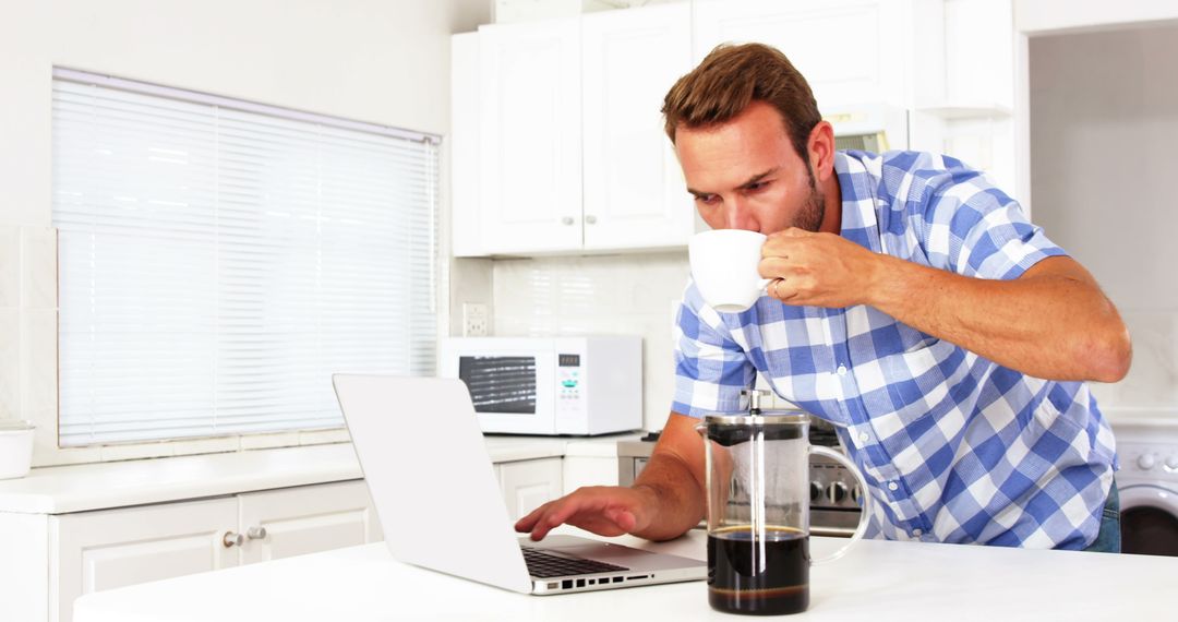 Man Drinking Coffee and Using Laptop in Modern Kitchen - Free Images, Stock Photos and Pictures on Pikwizard.com