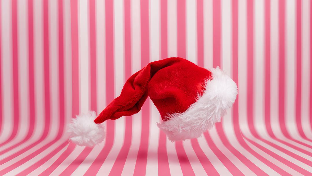 Floating Santa Hat Over Pink Striped Backdrop with Plush Fur Trim and Playful Pom-Pom
