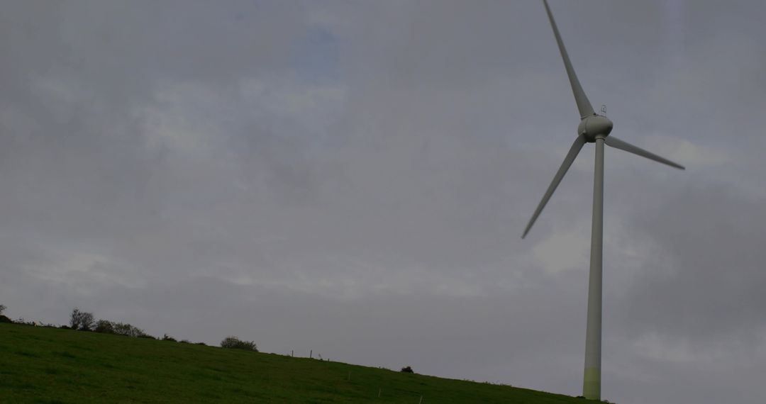 Solitary Wind Turbine on Green Hillside under Overcast Skies