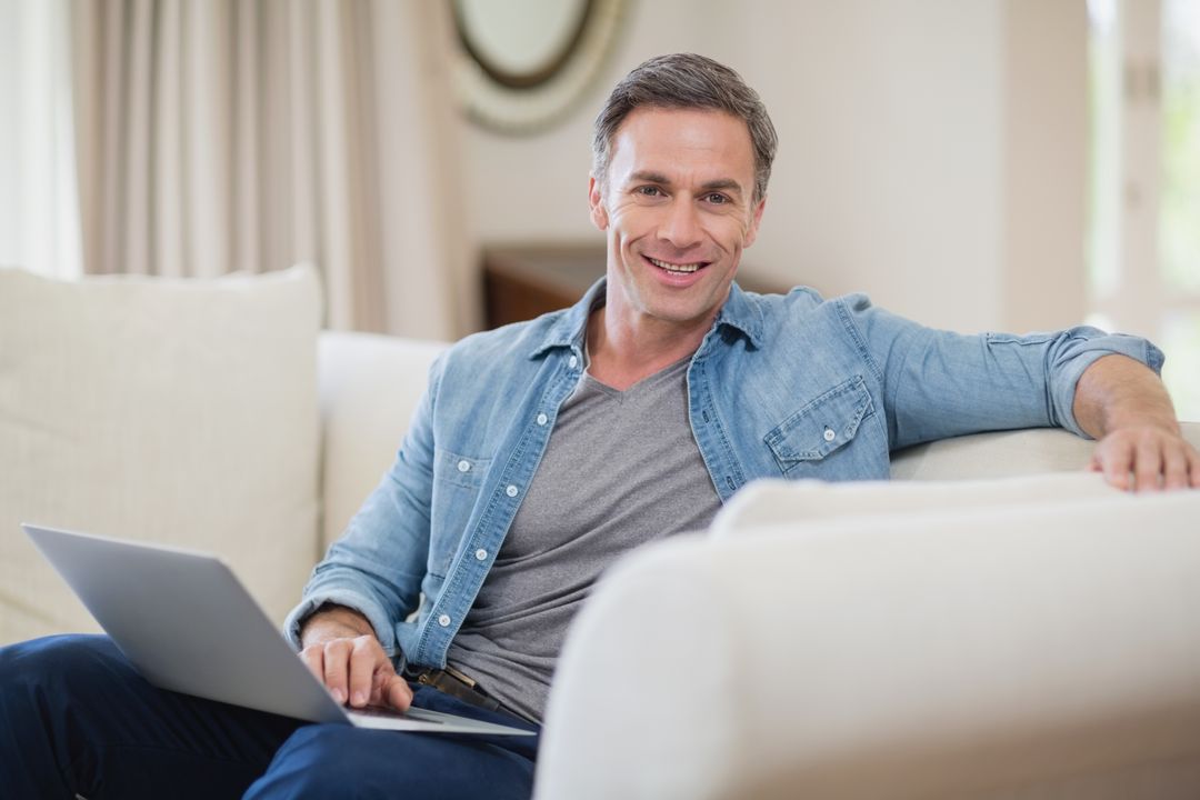Portrait of smiling man sitting on sofa with laptop in living room - Free Images, Stock Photos and Pictures on Pikwizard.com