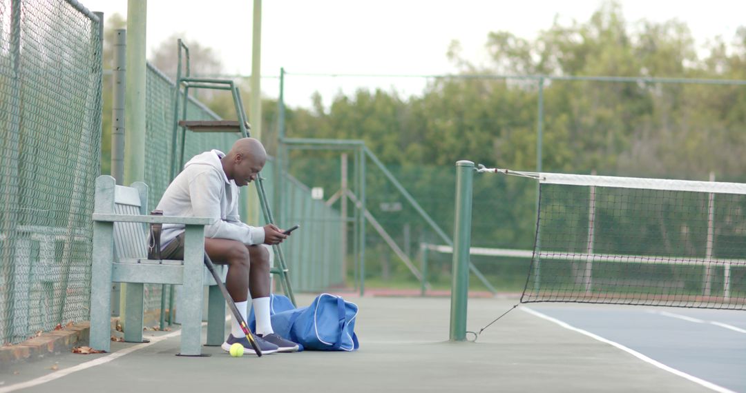 Tennis player sitting on bench checking phone at outdoor court - Free Images, Stock Photos and Pictures on Pikwizard.com