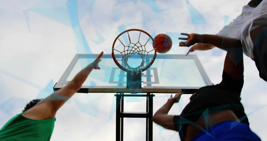 Low-angle action of leaping players reaching for basketball rim during outdoor street game