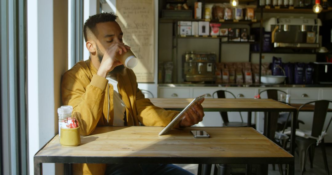 Young Man Enjoying Coffee While Using Digital Tablet in Cozy Café - Free Images, Stock Photos and Pictures on Pikwizard.com