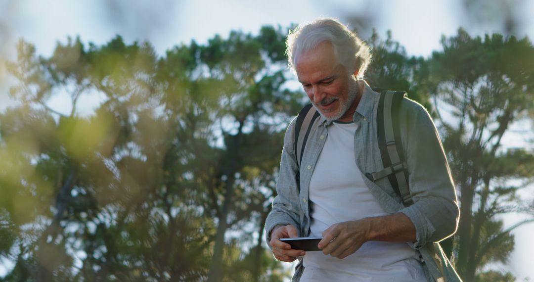 Senior Man Enjoying Nature and Using Smartphone in Forest - Free Images, Stock Photos and Pictures on Pikwizard.com