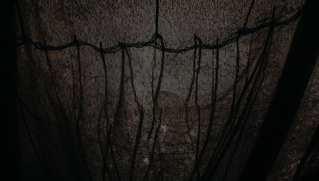 Hanging dark sheer curtain revealing vertical threads and textured folds backlit by window