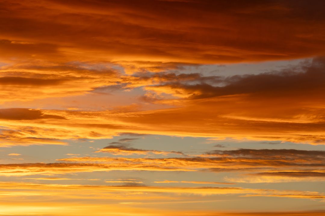 Fiery Sunset Clouds Painting Sky with Golden Orange and Soft Blue Layered Horizon