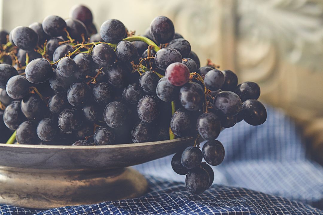 Dark Concord Grapes Resting on Rustic Metal Pedestal with Blue Checkered Cloth