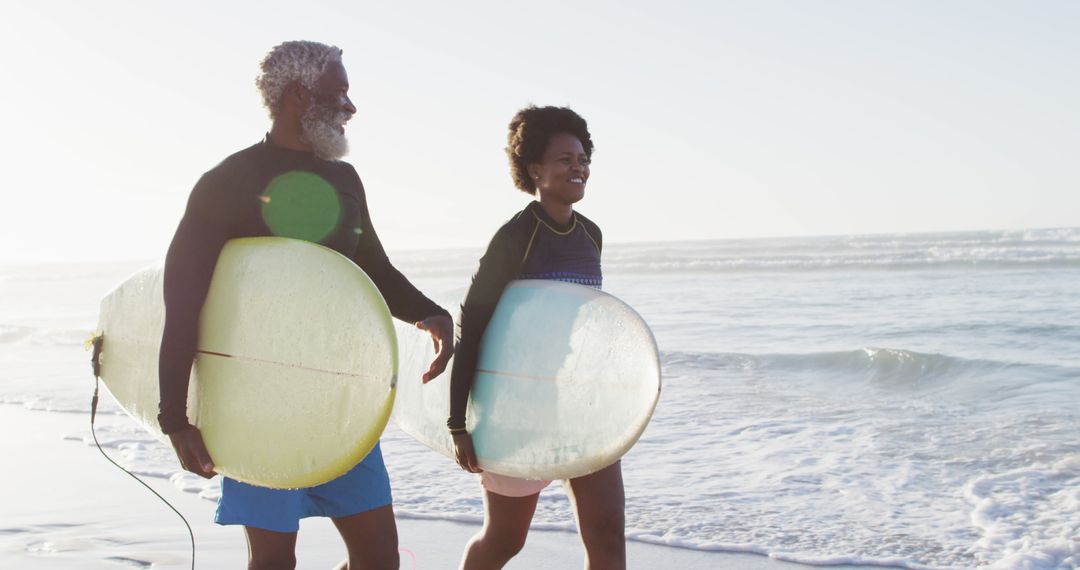 Happy african american couple walking with surfboards on sunny beach - Free Images, Stock Photos and Pictures on Pikwizard.com