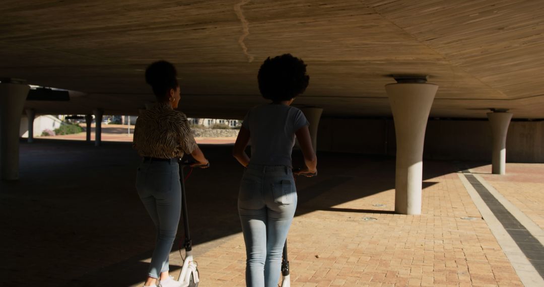 Two Women Riding Electric Scooters Under Bridge - Free Images, Stock Photos and Pictures on Pikwizard.com