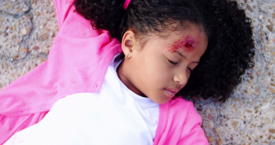 Injured Child Lying on Ground with Forehead Wound in Pink Jacket - Free Images, Stock Photos and Pictures on Pikwizard.com